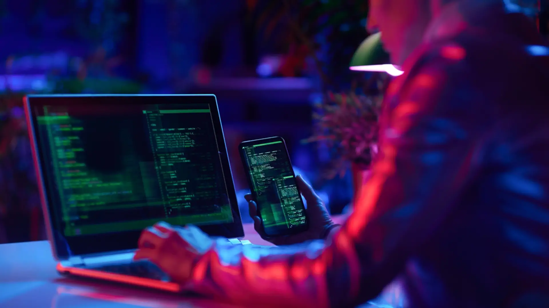 Personne consultant du code malveillant sur un smartphone et un ordinateur portable lors d’une cyberattaque