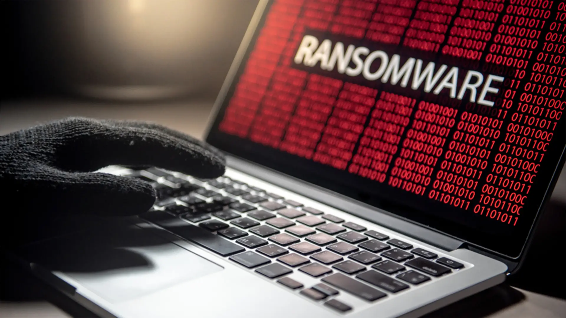 Main gantée tapant sur un clavier d’ordinateur affichant le mot "RANSOMWARE" à l’écran