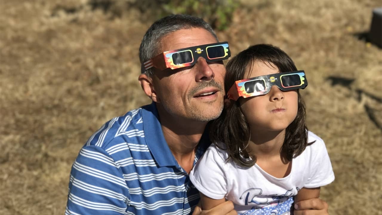 Un père et sa fille qui observent une éclipse solaire avec des lunettes de protection