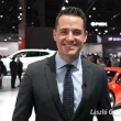 Homme souriant dans un faux salon automobile généré par l’IA Veo 3 de Google