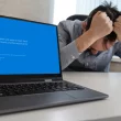 Un écran bleu de la mort (BSOD) affiché sur un PC portable, avec un utilisateur frustré en arrière-plan