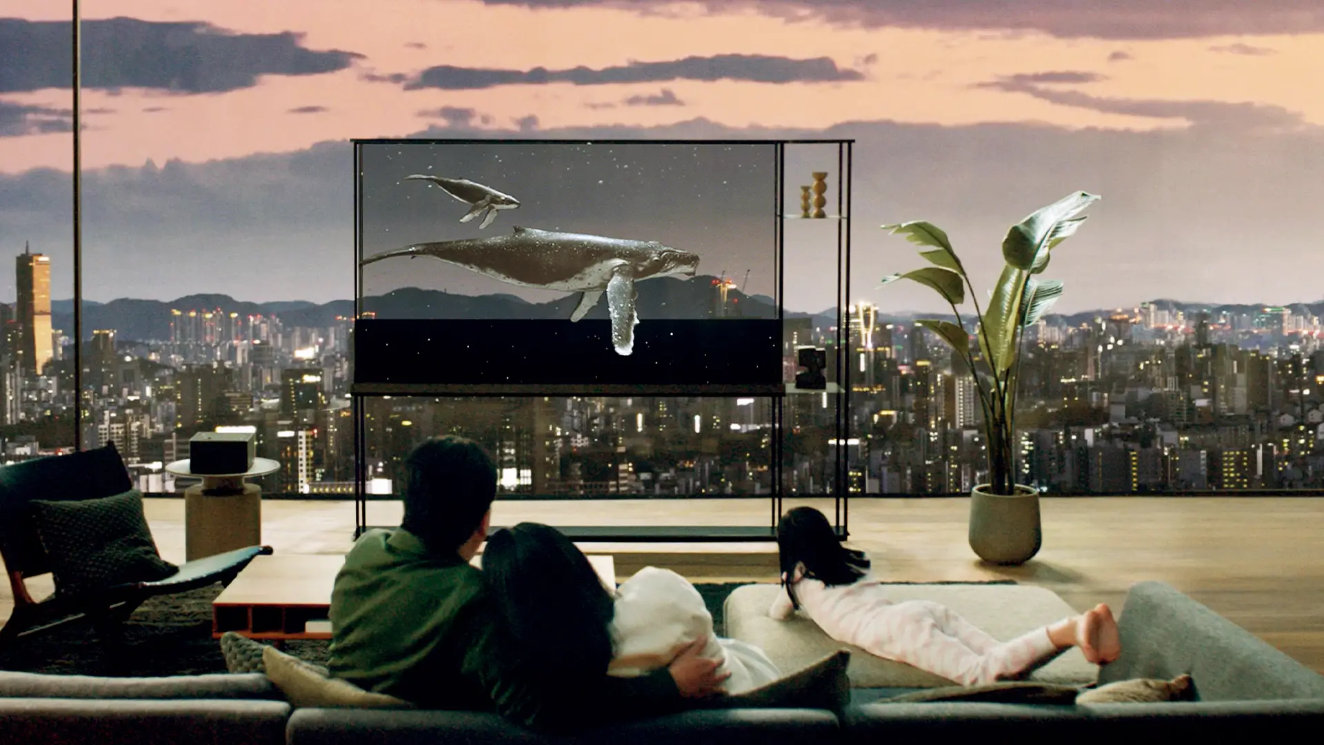Famille regardant une TV LG OLED T transparente dans un salon avec vue panoramique sur la ville