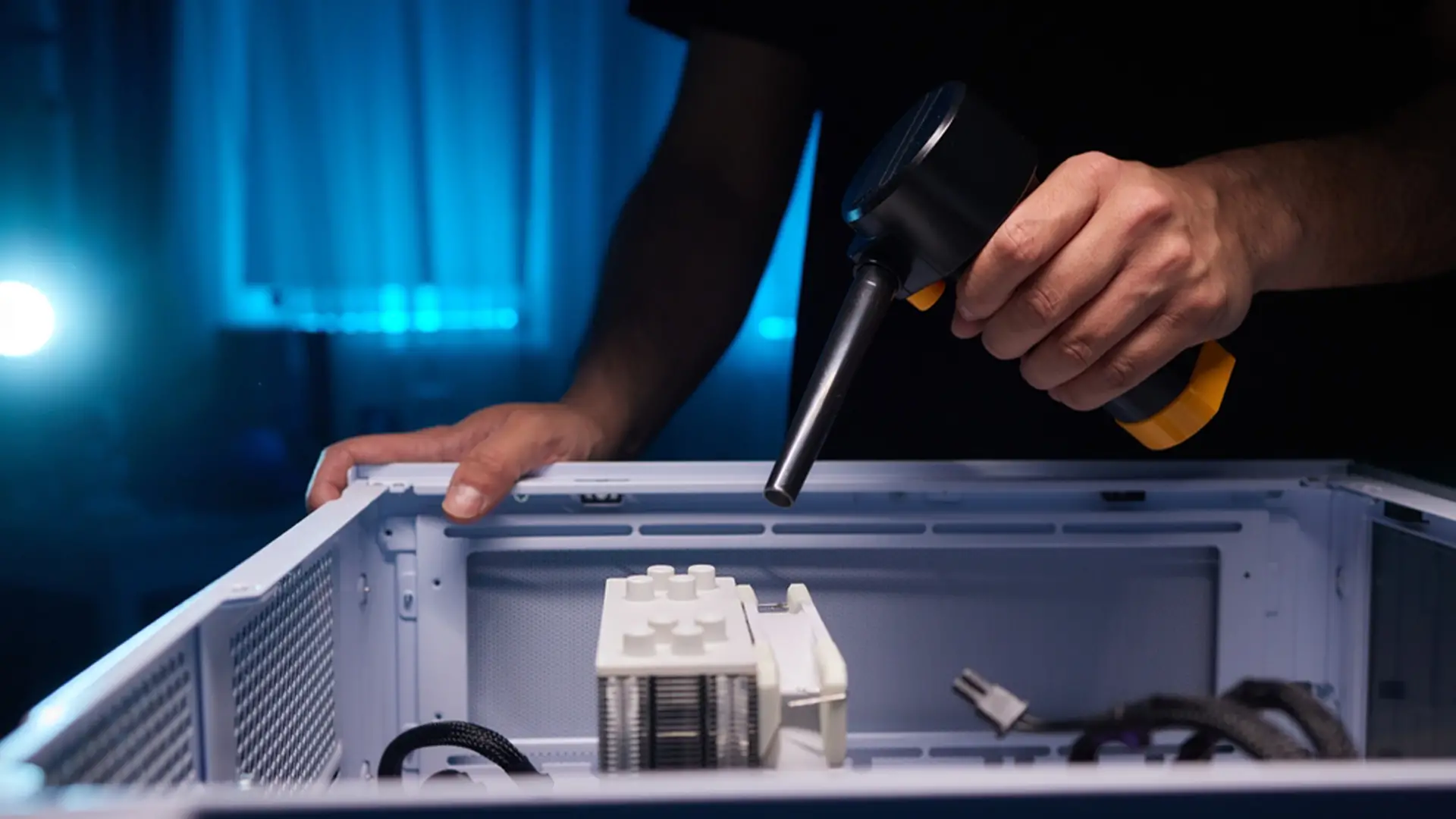 Nettoyage de l’intérieur d’un PC fixe avec un souffleur électrique dans une pièce sombre.