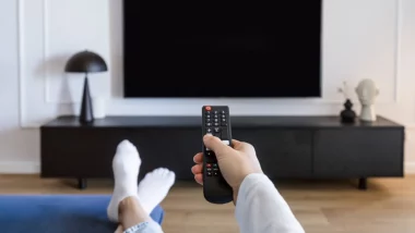 Personne tenant une télécommande face à un téléviseur éteint – changement des chaînes de la TNT le 6 juin 2025
