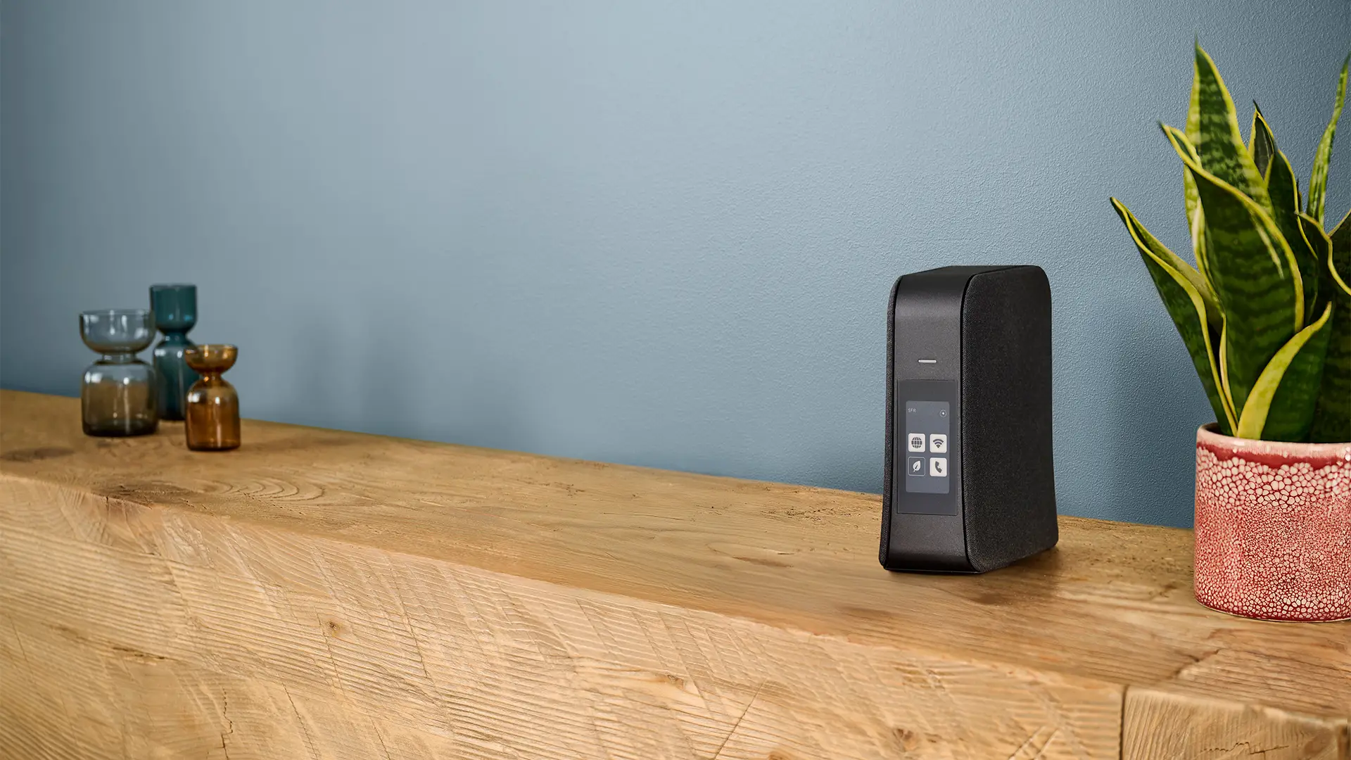 La Box 10+ de SFR posée sur un meuble en bois, à côté de plantes et objets déco
